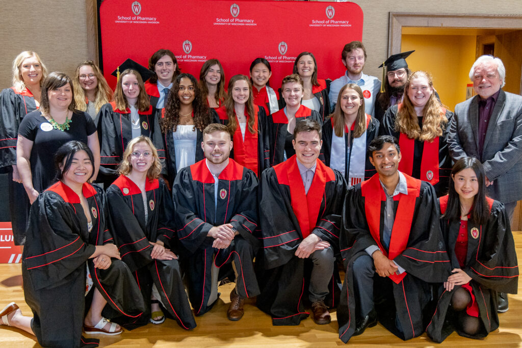 The 2023 PharmTox class poses in front of the red School of Pharmacy background.