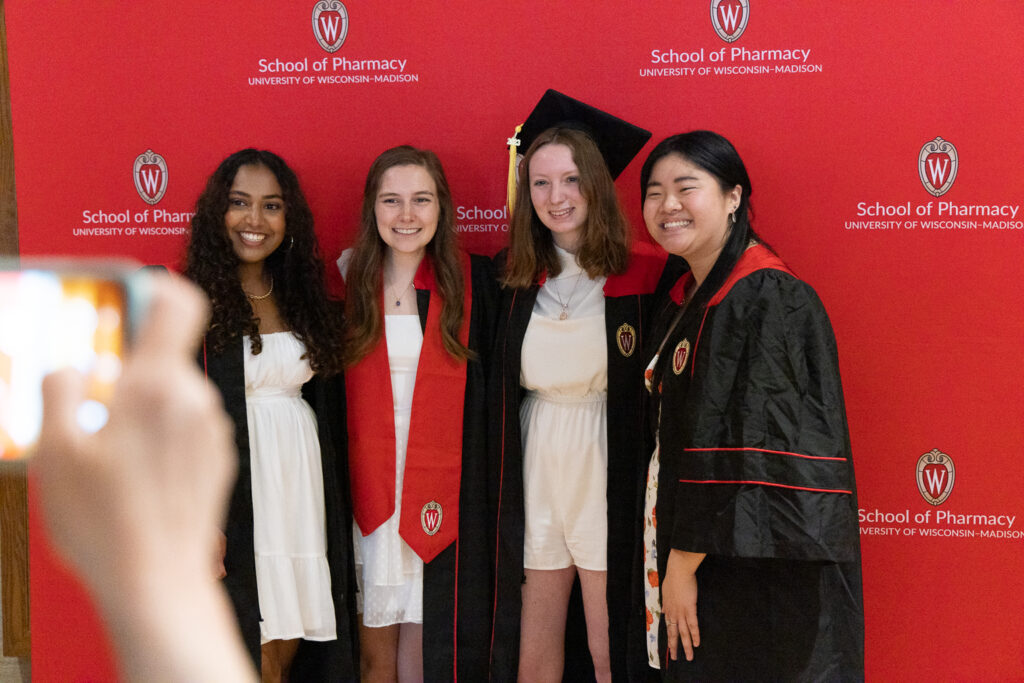 PharmTox graduates posing in front of a red School of Pharmacy backdrop.