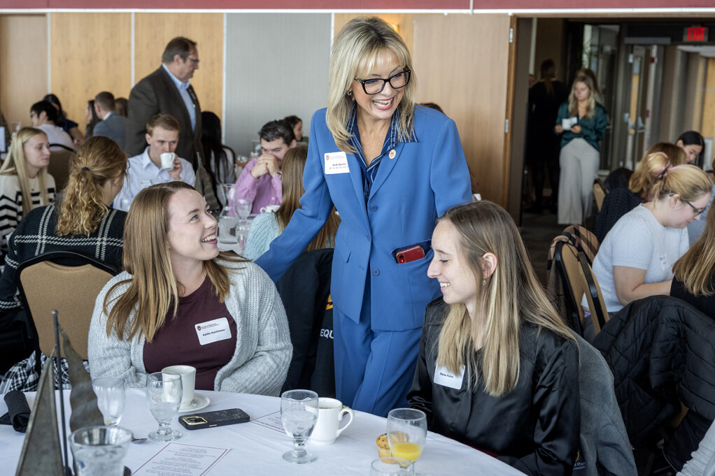 Beth Martin standing over and smiling with Kaitlin Hutchinson and Alyssa Kuhn who are seated