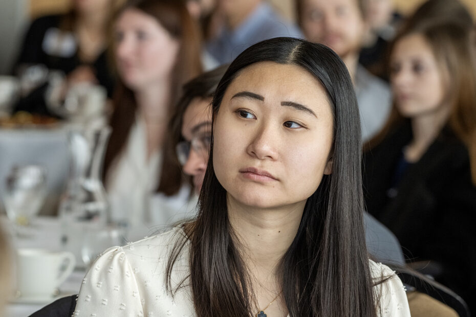 Camera focused on Jenny Lin straight-faced listening to speaker with everyone behind her out of focus