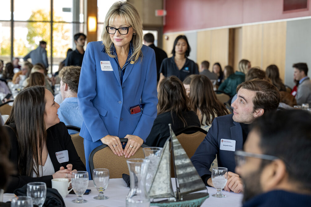 Beth Martin standing and resting hands against empty chair while speaking to seated students