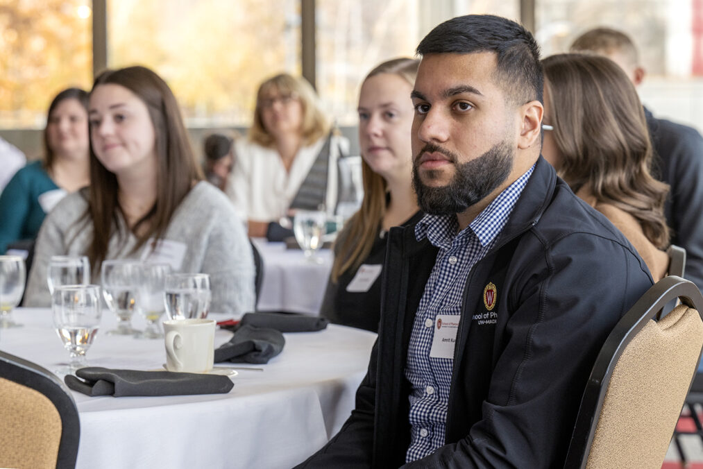 Camera focused on Amrit Kumar sitting and listening to speaker with students behind him out of focus