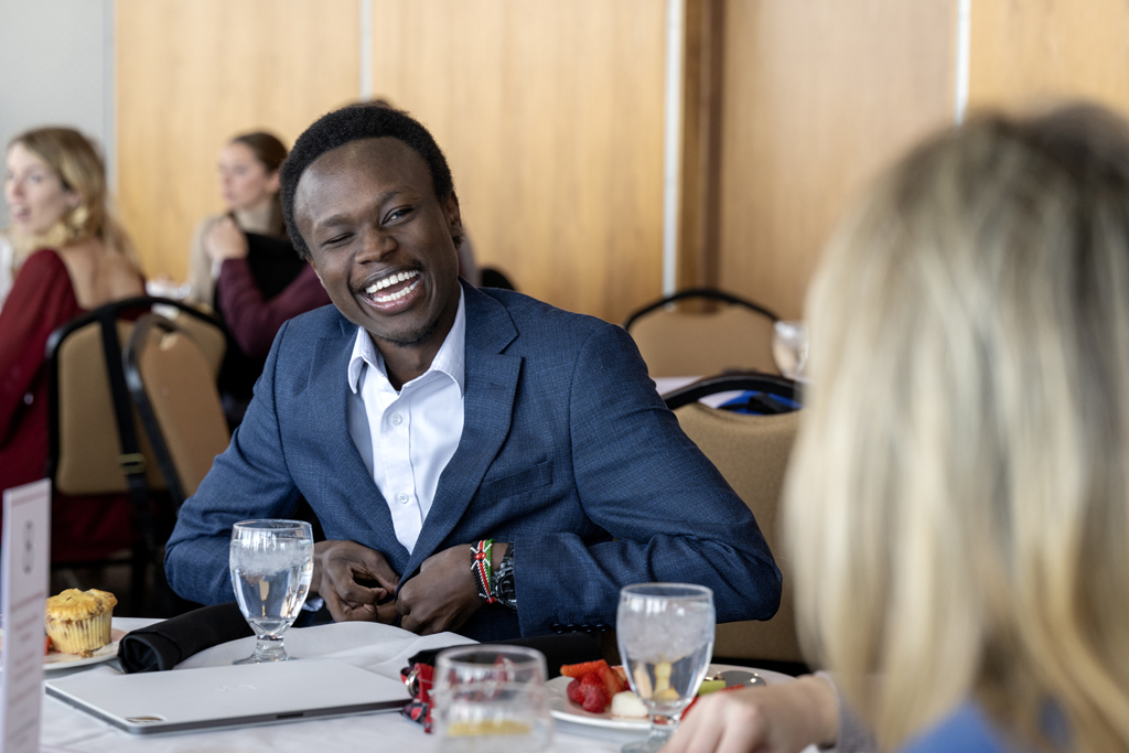 Camera focused on Vincent Elijah laughing as he speaks with Beth Martin while sitting around table