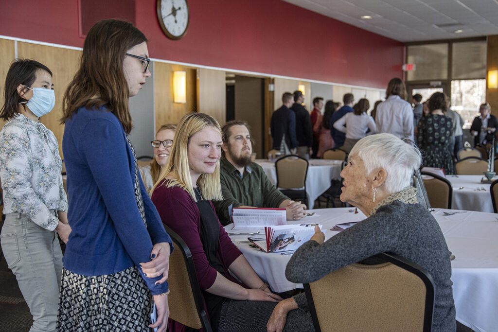 PharmD Student Scholarship Brunch_042021_BGI_6068 PharmD student Marissa Hakala (standing) listens with classmate Stacy Soltis (seated) as her great Aunt Liz Allen talks to them during the 2022 School of Pharmacy Scholarship Brunch