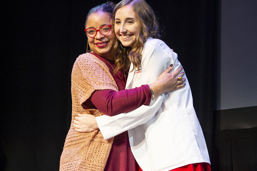 Student in white coat hugging staff during white coat ceremony