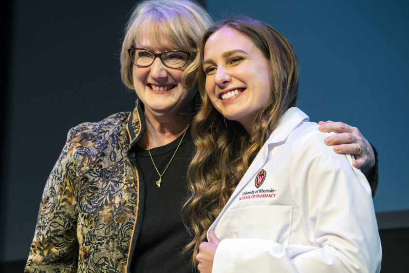 Student wearing white coat taking picture with staff during white coat ceremony
