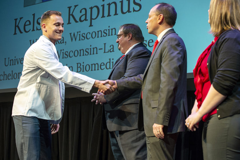 Student wearing white coat and shaking staff's hand