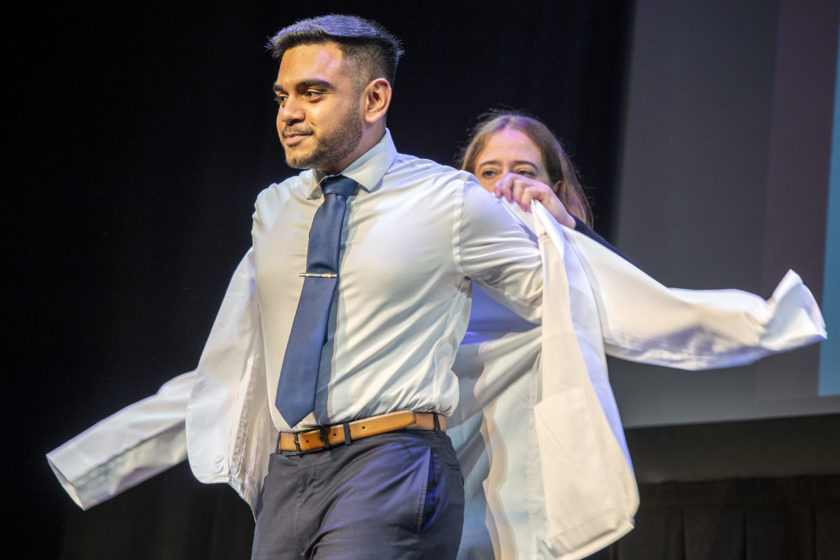 Staff helping student put on white coat during white coat ceremony
