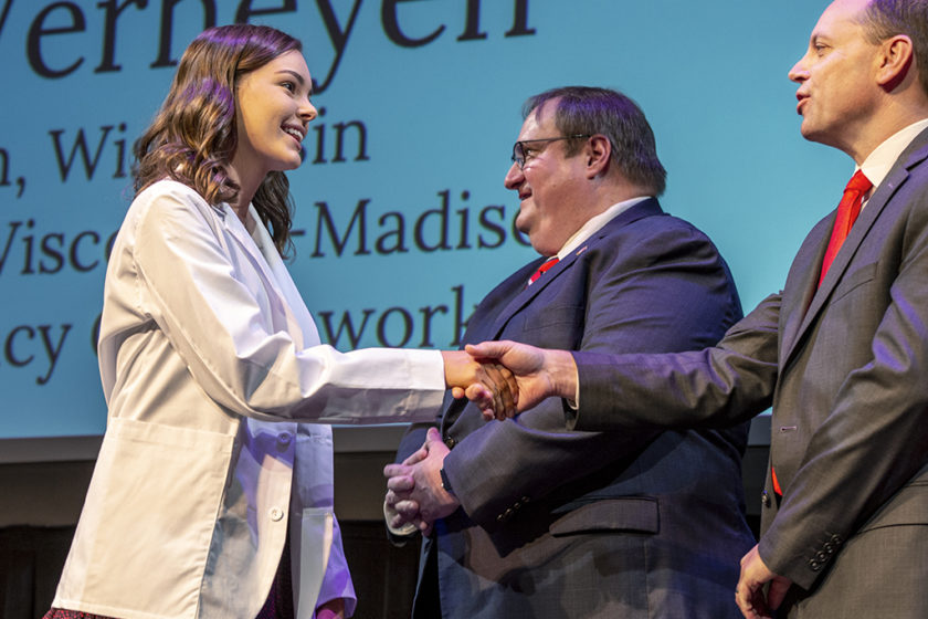 Student wearing white coat and shaking staff's hand