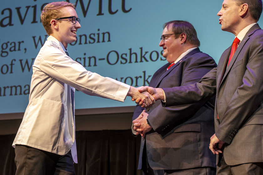 Student wearing white coat and shaking staff's hand