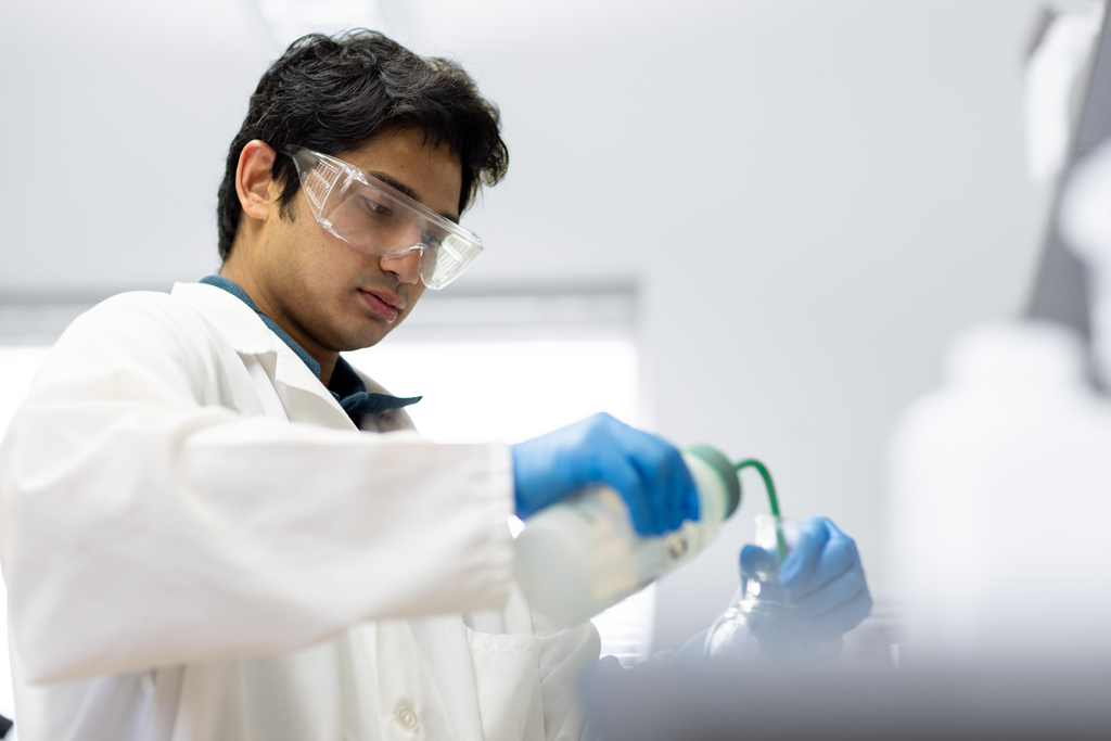 Uriel Matthew Enriquez, a graduate student in the Pharmaceutical Sciences PhD Program, washes a round-bottom flask with acetone.