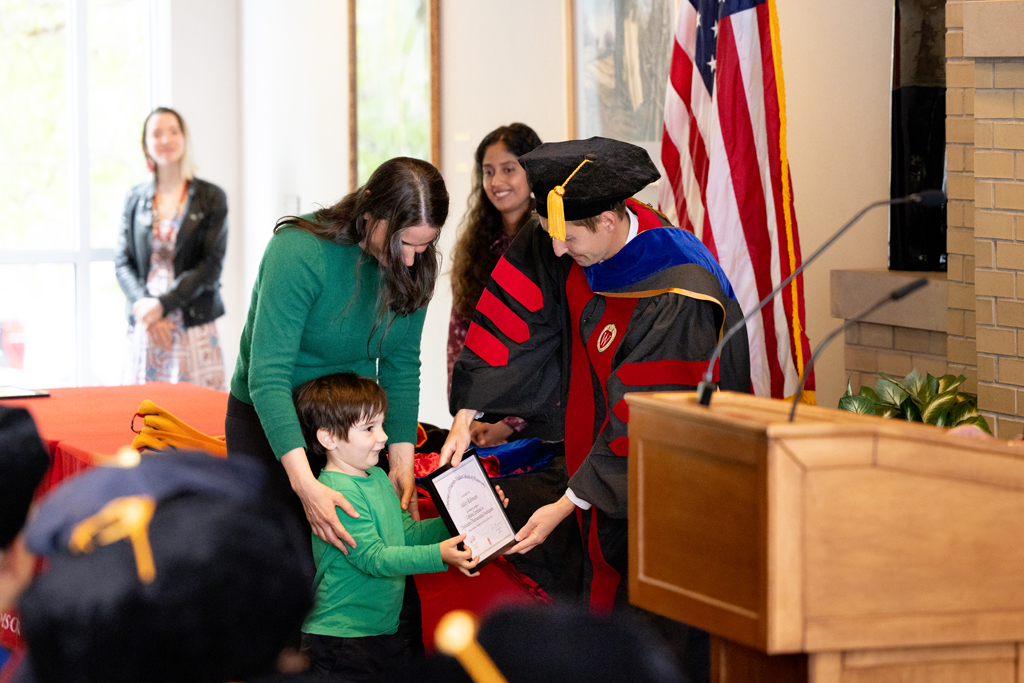 Pharmacy_Graduation_2024_067 A small boy is handed a plaque with his mom