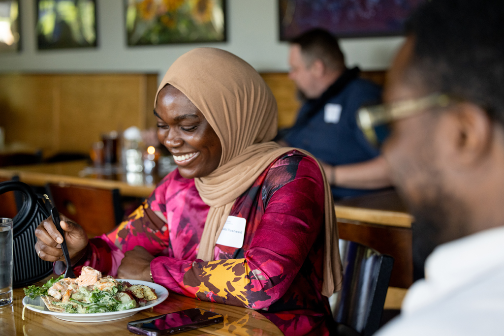 An alum in a head wrap smiles over a plate of food