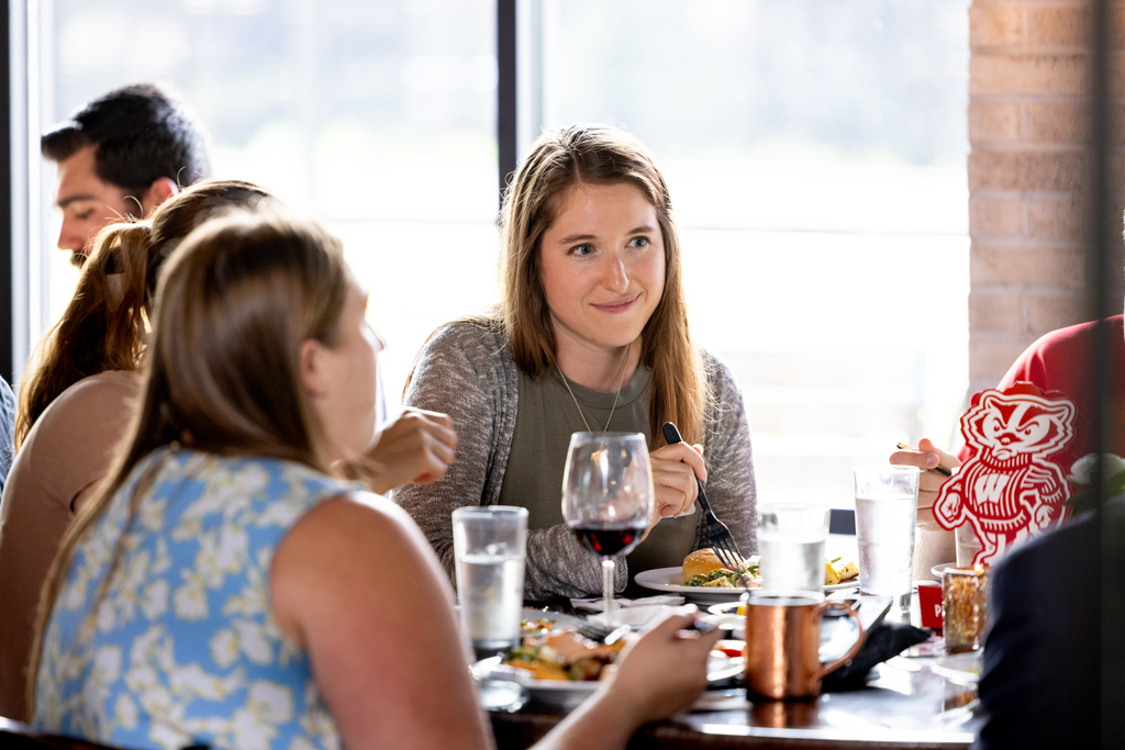 An alum smiles at others while eating