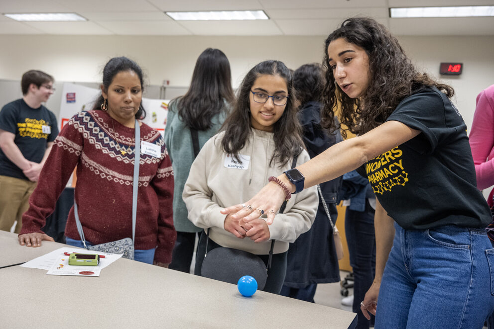 The Wonders of Pharmacy_032024_PLNZ72_7326 First-year PharmD student Nourhan El-Sanjak, right, explains where to roll the ball for a high score to Kavya Kashyap as her mother, Lalitha Kashyap, looks on as she plays the Pharmacy Pipeline activity during the Wonders of Pharmacy.