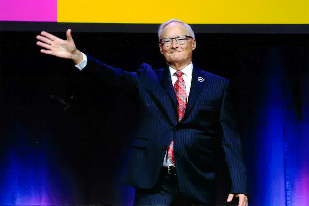 Tom Thielke on a stage waving his arm.