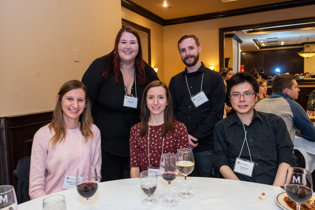 UW-Pharm-Maggianos_20220426__DSC2496_054 Alumni standing and sitting behind a table for a picture