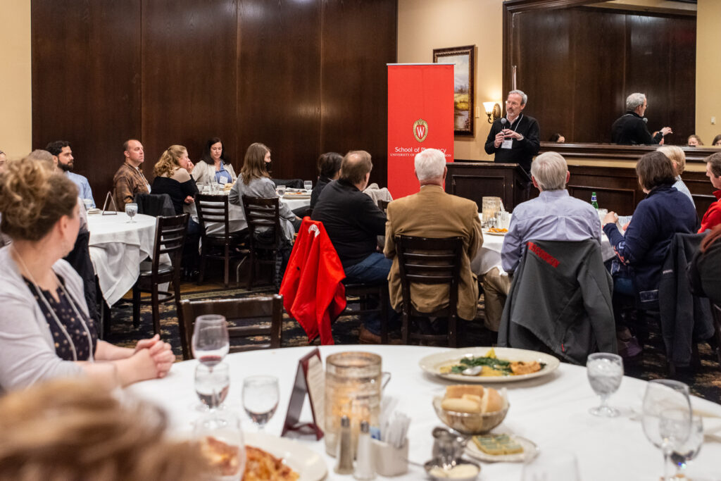 UW-Pharm-Maggianos_20220426__DSC2501_057 Dave Mott speaking at the podium with tables of people listening to him