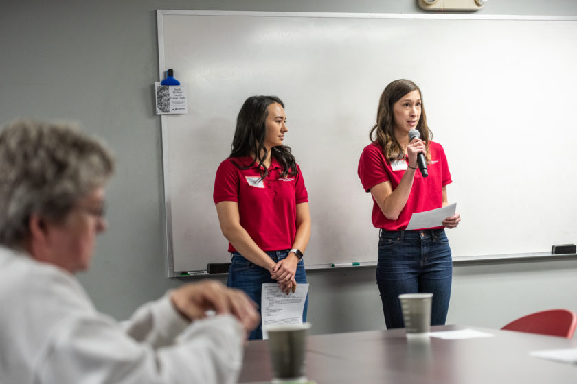 Two women wearing red School of Pharmacy shirts with one holding a microphone