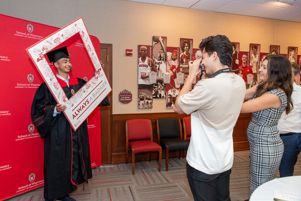 UWPhrmToxAw_2022_201 Graduated student standing in front of a red backdrop using frame prop