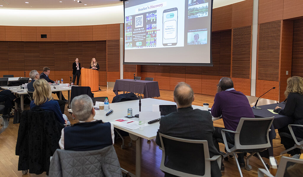 Alexis Doering and Elle Noone present in front of a large screen showing a Powerpoint presentation