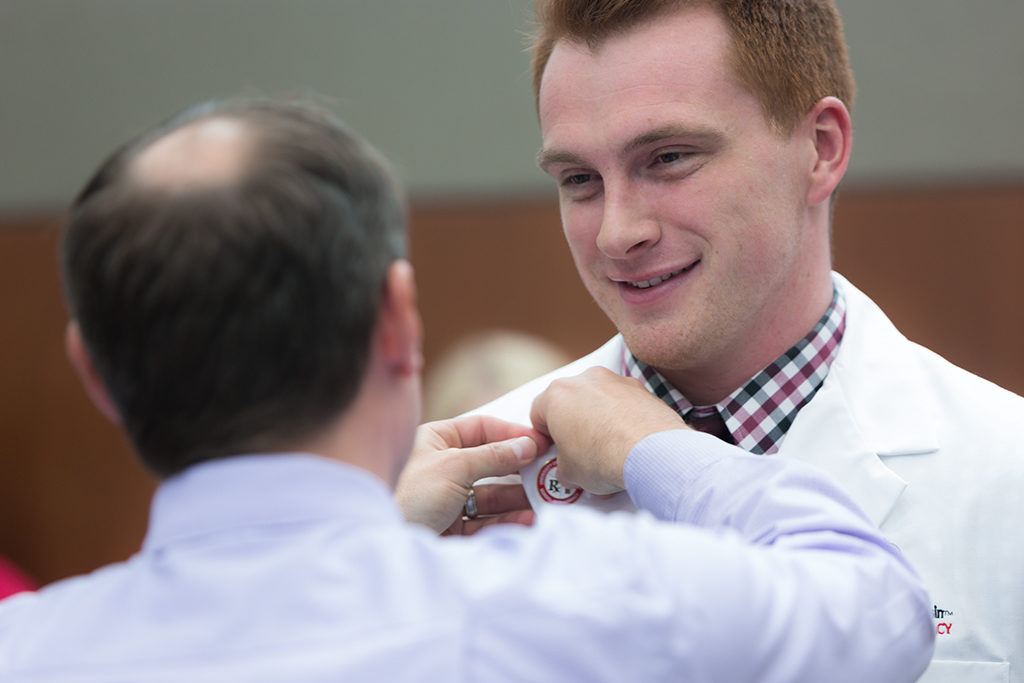 phar050219_004 Student accepts pin from Jason Law, alumni of the School.