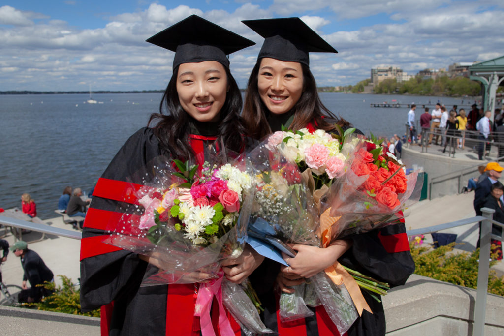 phar051019_006 Two graduated students holding large bouquets together