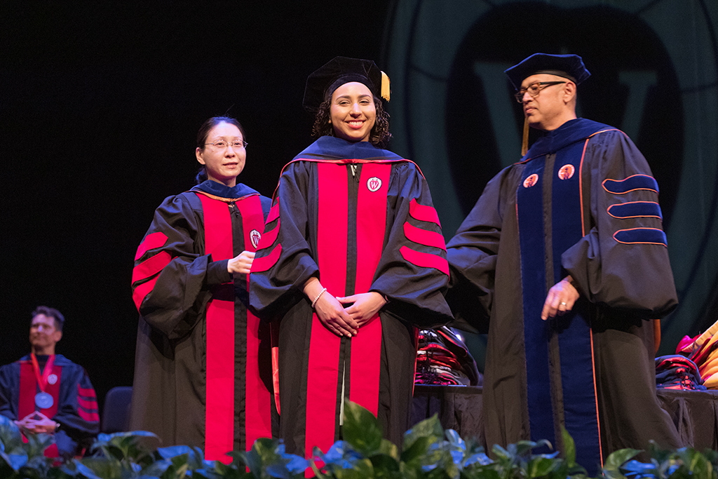 Faculty place a hood over a graduate's head.