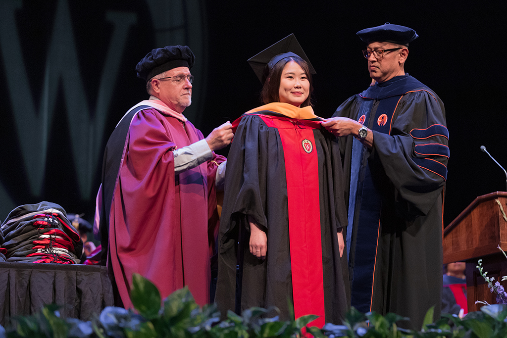Faculty place a hood over a graduate's head.
