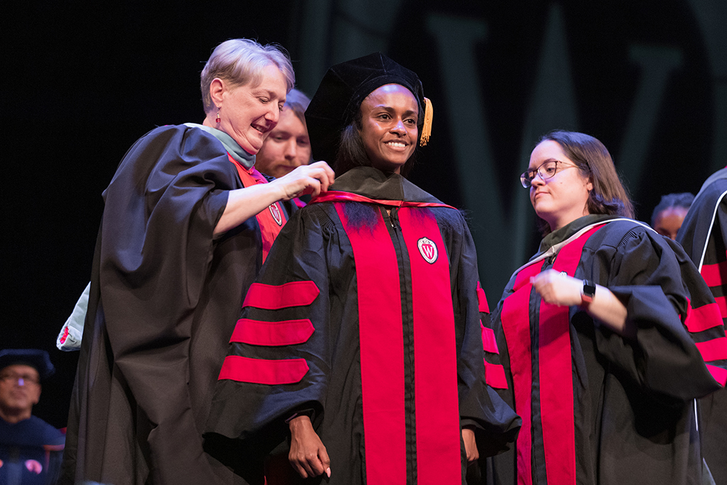 Faculty place a hood over a graduate's head.