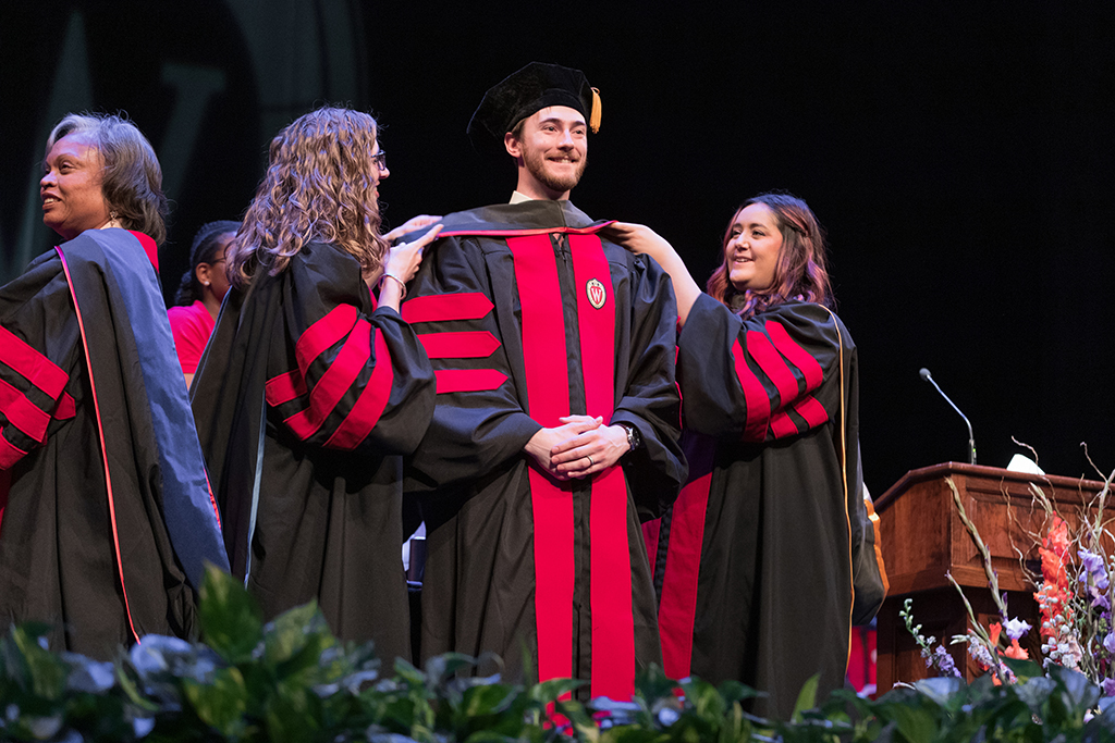 Faculty place a hood over a graduate's head.