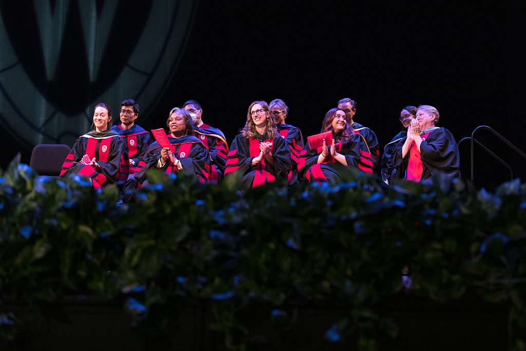 A group of faculty applaud onstage.
