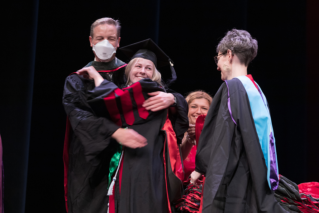 Two pharmacy professors bestowing a hood upon a graduate student at the hooding ceremony
