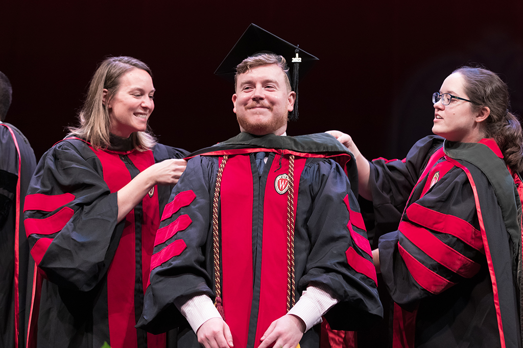Class of 2022 PharmD graduate Jeff Wirtz receives his hood from professors Kate Rotzenburg and Amanda Margolis