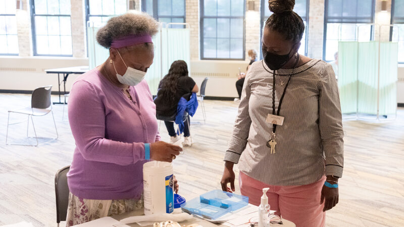 AAHN Outreach and Vaccination Clinic with Eva Vivian, PharmD, MS, PhD Professor Eva Vivian and Letesha Nelson standing in large open clinic with table full of supplies