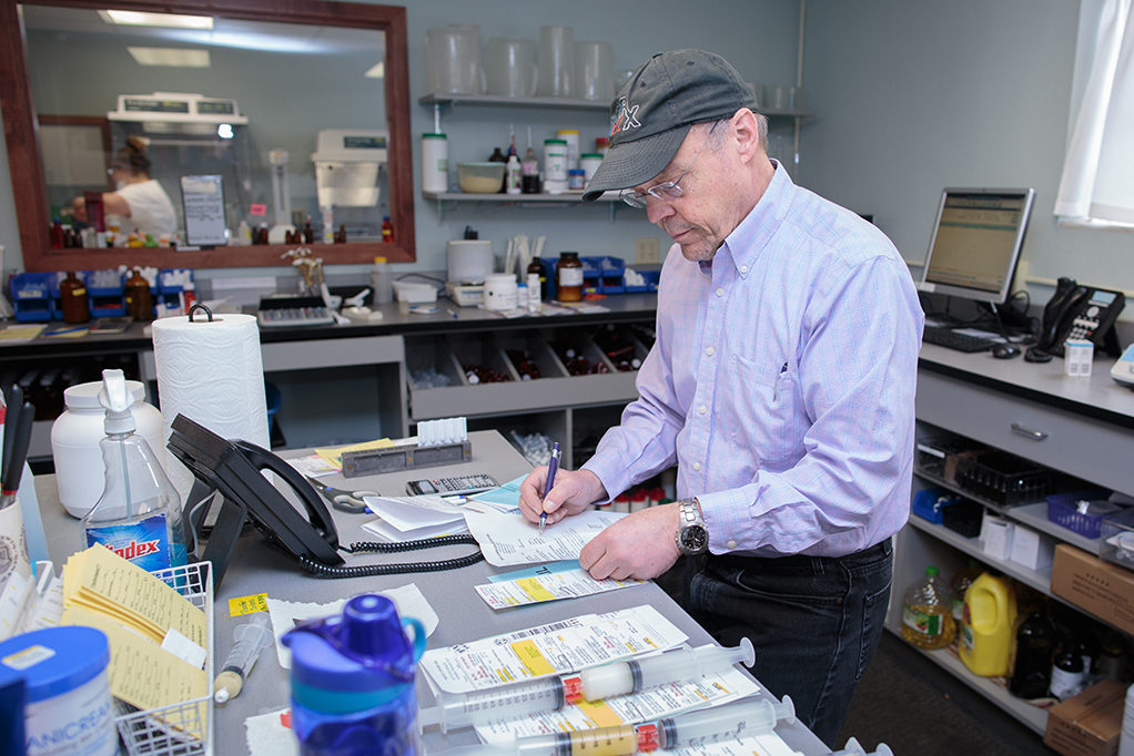 phar052218_044 Jeff Langer working with counter full of prescriptions and syringes