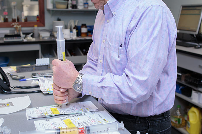 phar052218_045 Jeff Langer working at counter with prescriptions and syringes