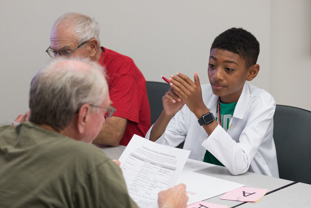 SoP Grandparents University 2023 A young boy smiles and looks on as an older attendee reviews a worksheet