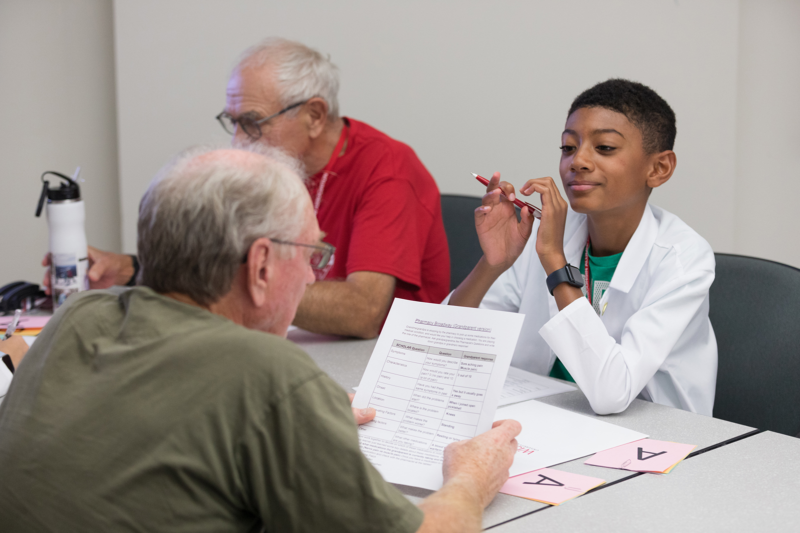 A young boy smiles and looks on as an older attendee reviews a worksheet