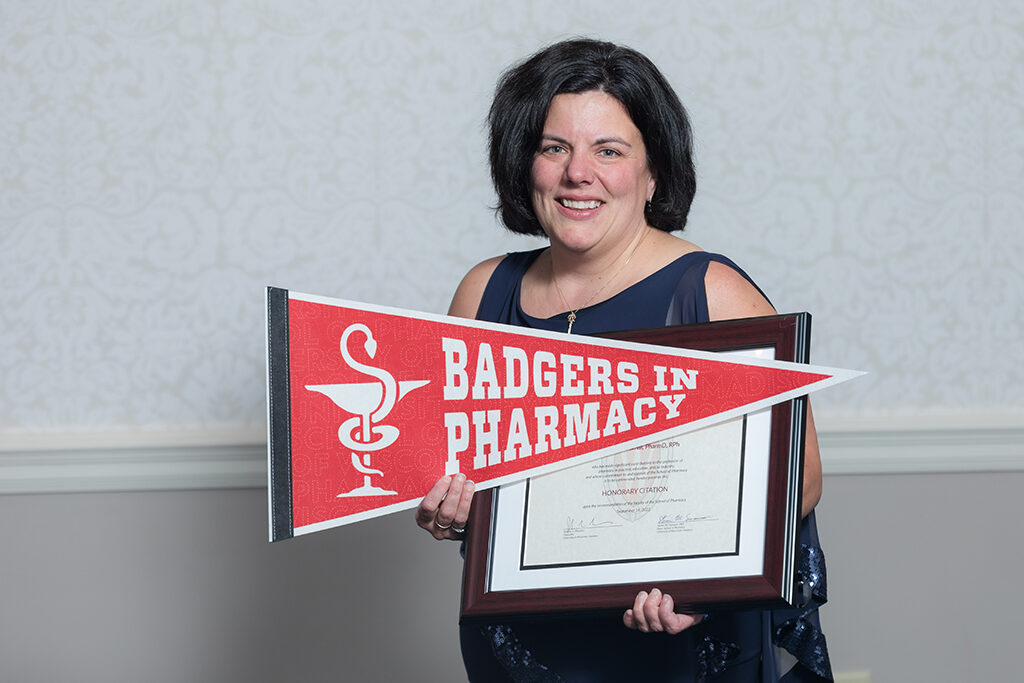 UW School of Pharmacy 2022 Citations of Merit Dinner & Awards Michelle Farrell with her Citation award and a Badgers in Pharmacy pennant flag.