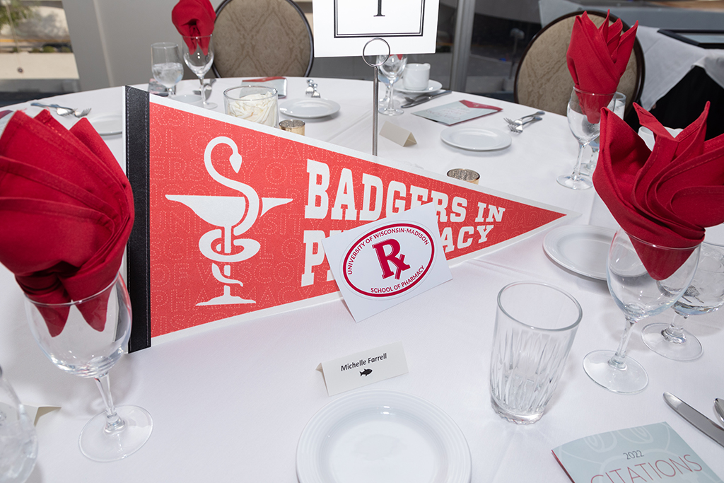 UW School of Pharmacy 2022 Citations of Merit Dinner & Awards A table setting for Michelle Farrell, with a pennant flag, Rx School of Pharmacy Sticker, and empty dishes.