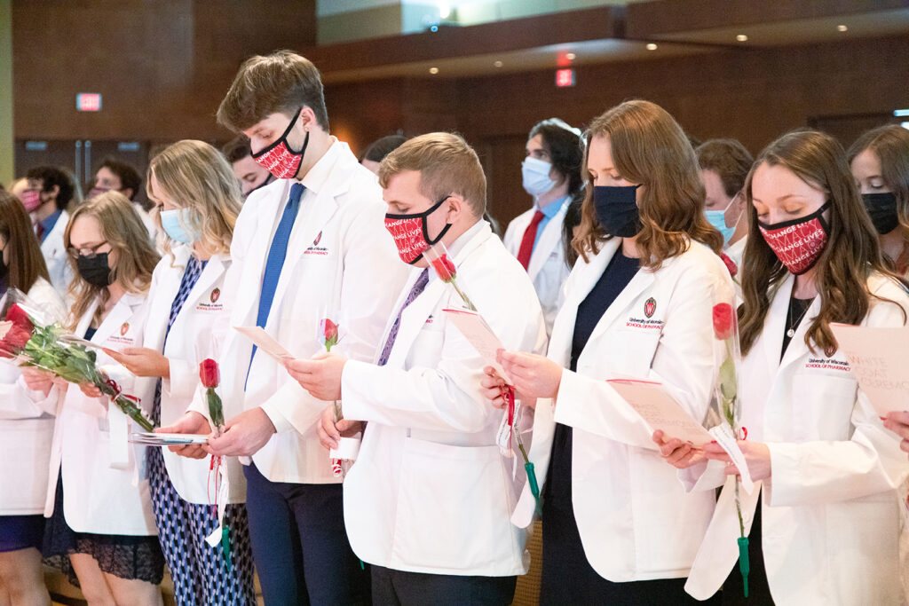 Pharm students holding roses and white coat ceremony pamphlets