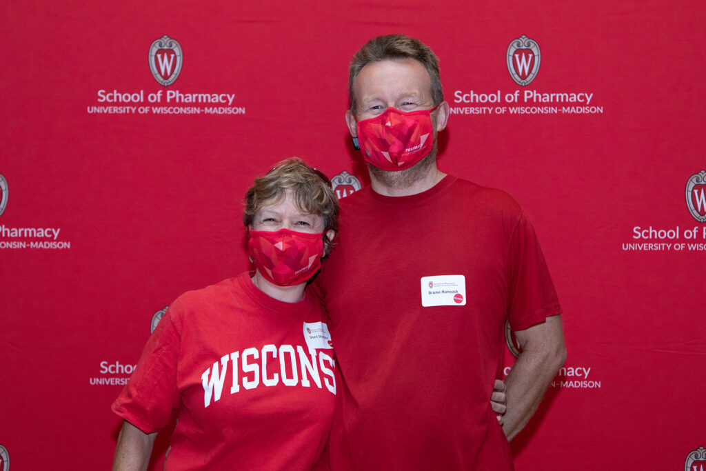 School of Pharmacy Alumni Tailgate Party 2021 Two pharmacy alumni standing in front of red School of Pharmacy backdrop