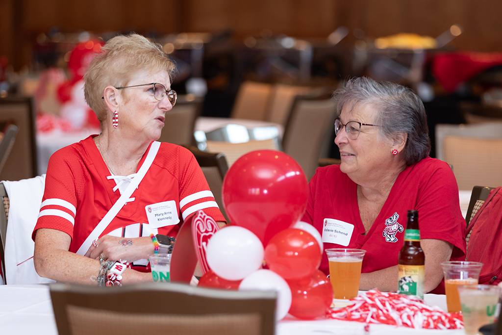 UW–Madison School of Pharmacy 2024 Alumni Tailgate and Watch Party Mary Anne Kennedy and Valerie Schend speak at a table decorated with balloons