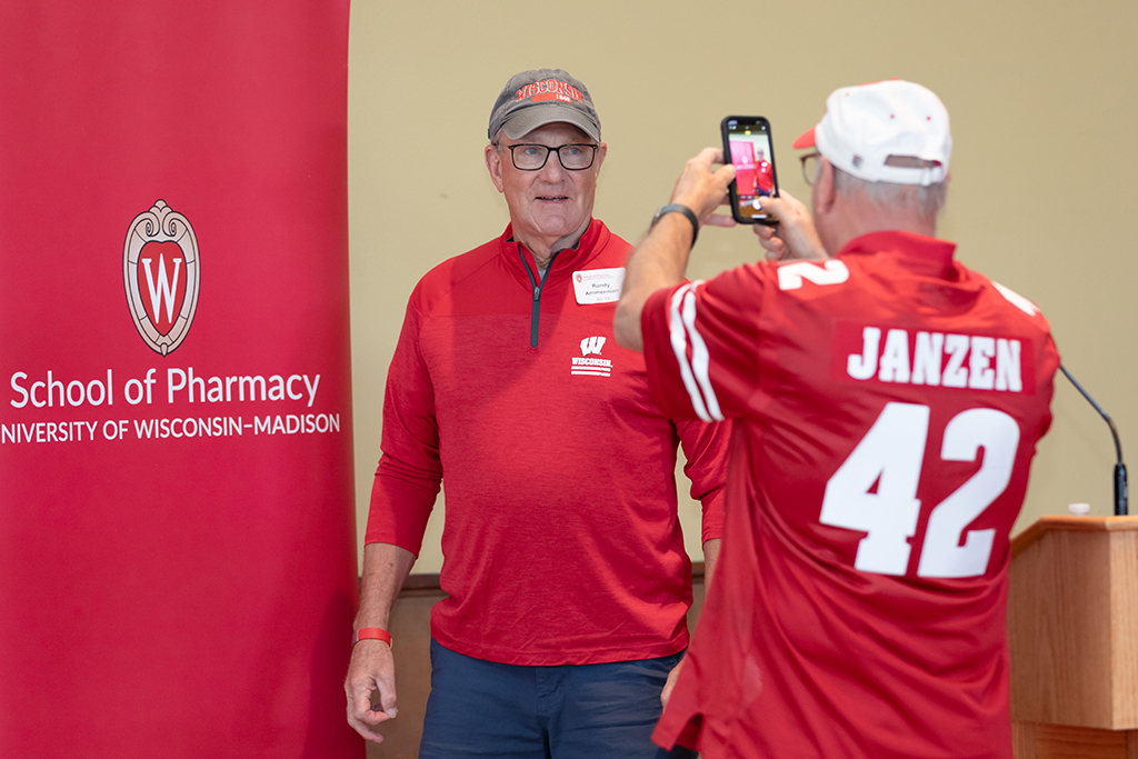 UW–Madison School of Pharmacy 2024 Alumni Tailgate and Watch Party Kie Janzen takes a photo of Randy Ammerman in front of the School of Pharmacy banner