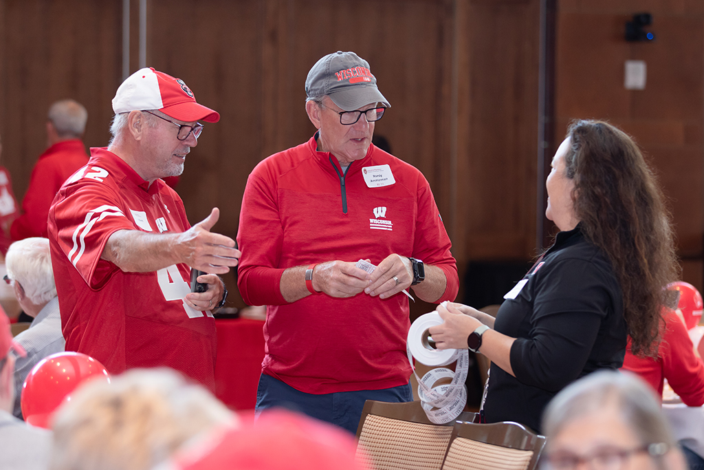 UW–Madison School of Pharmacy 2024 Alumni Tailgate and Watch Party Kie Janzen and Randy Ammerman speak with Julie Bartell, who is holding a roll of raffle tickets