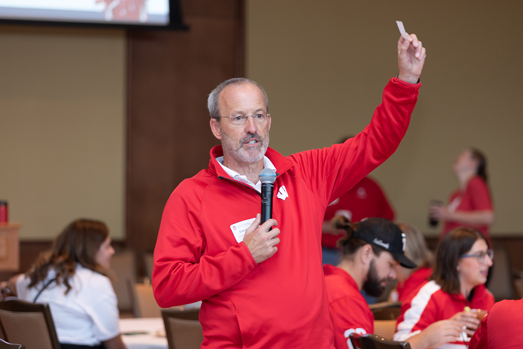 UW–Madison School of Pharmacy 2024 Alumni Tailgate and Watch Party Dave Mott speaks into a microphone with his hand holding a raffle ticket in the air.
