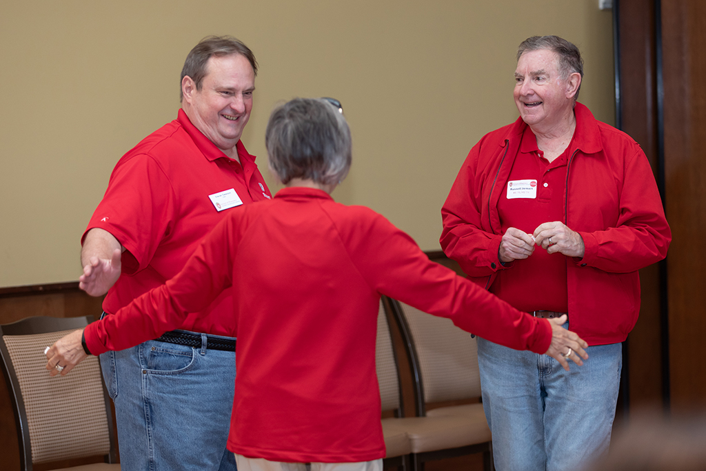 UW–Madison School of Pharmacy 2024 Alumni Tailgate and Watch Party A female alum, facing away from the camera with arms spread, speaks with a smiling Steve Swanson and Russ Jensen.