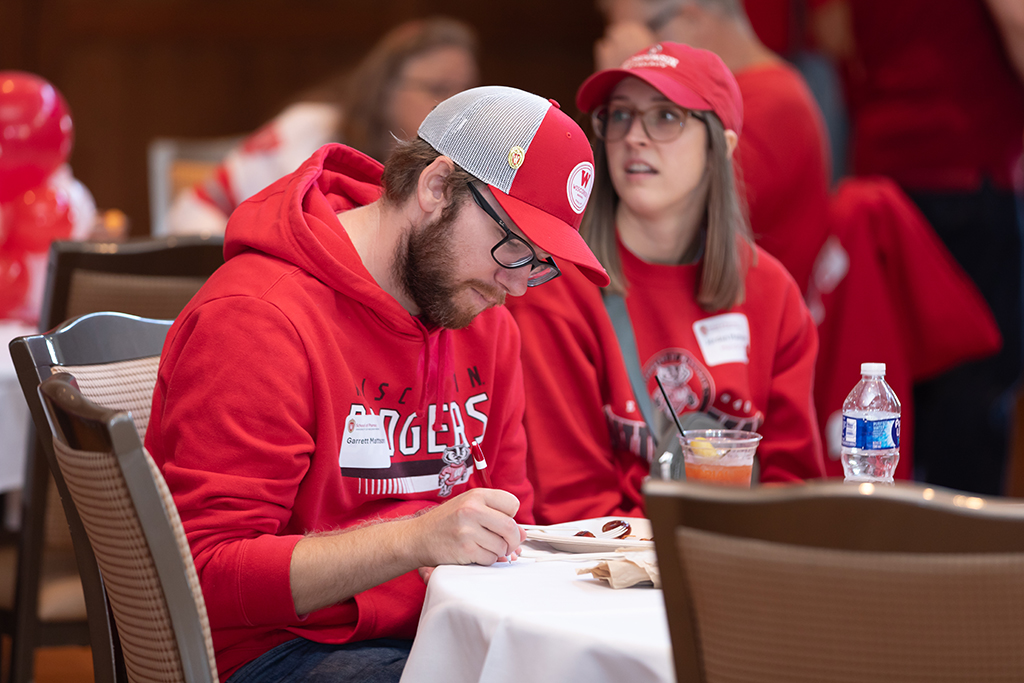 UW–Madison School of Pharmacy 2024 Alumni Tailgate and Watch Party Garrett Mattson writes something at a table next to Jordan Mattson
