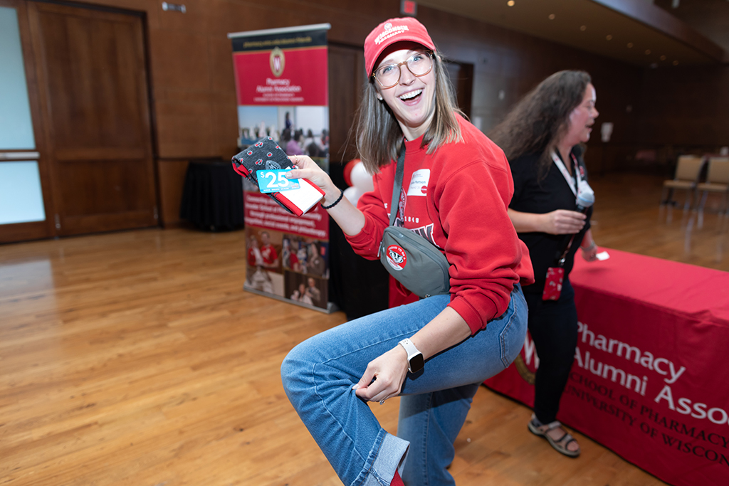 UW–Madison School of Pharmacy 2024 Alumni Tailgate and Watch Party An alum holds up a $25 gift card and shows off her Badger socks